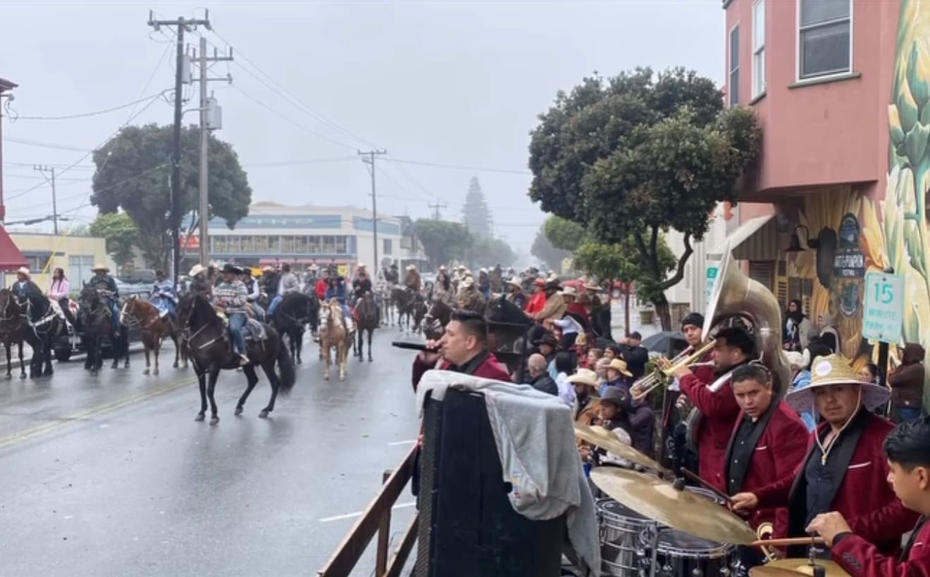 A banda performing on the street as riders pass by in the rain