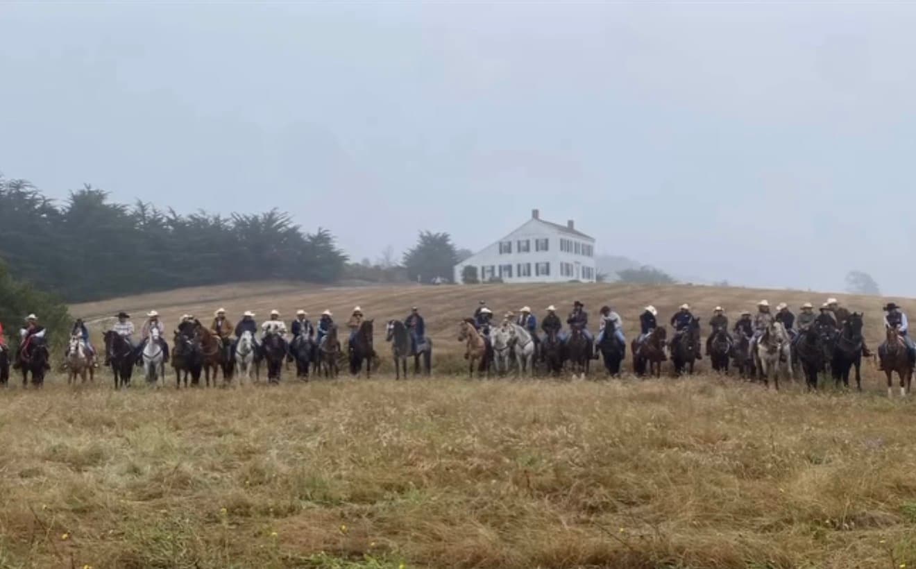 A line of riders on horseback in the fog in front of the historic Johnston House