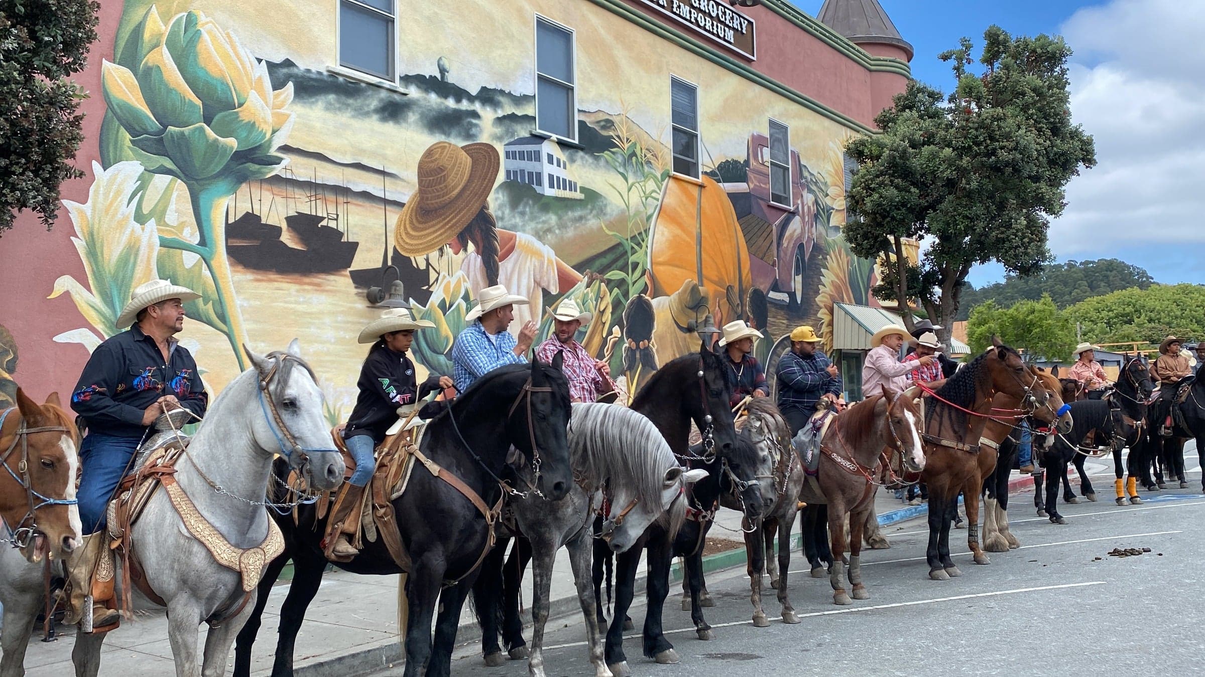Riders on horseback in front of a colorful mural on Main Street on a sunny day