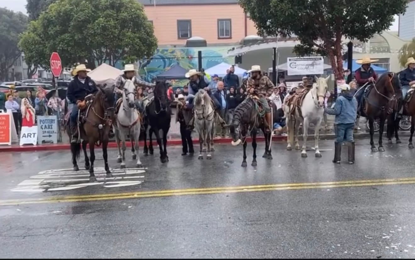 Riders on horseback passing a crowd on a rainy Main Street