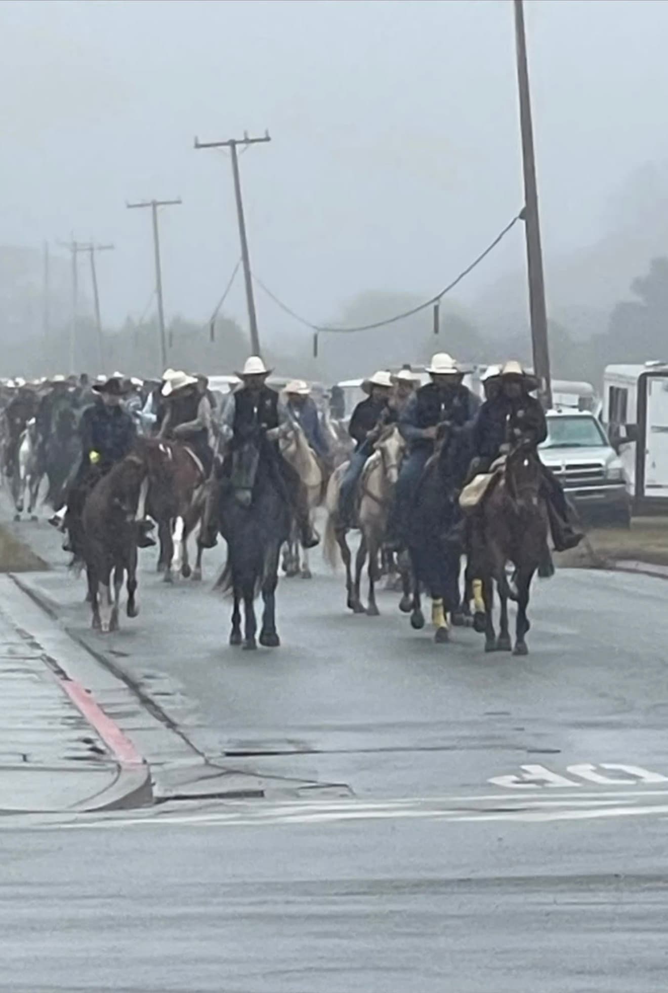 A long line of riders on horseback moving down a foggy road